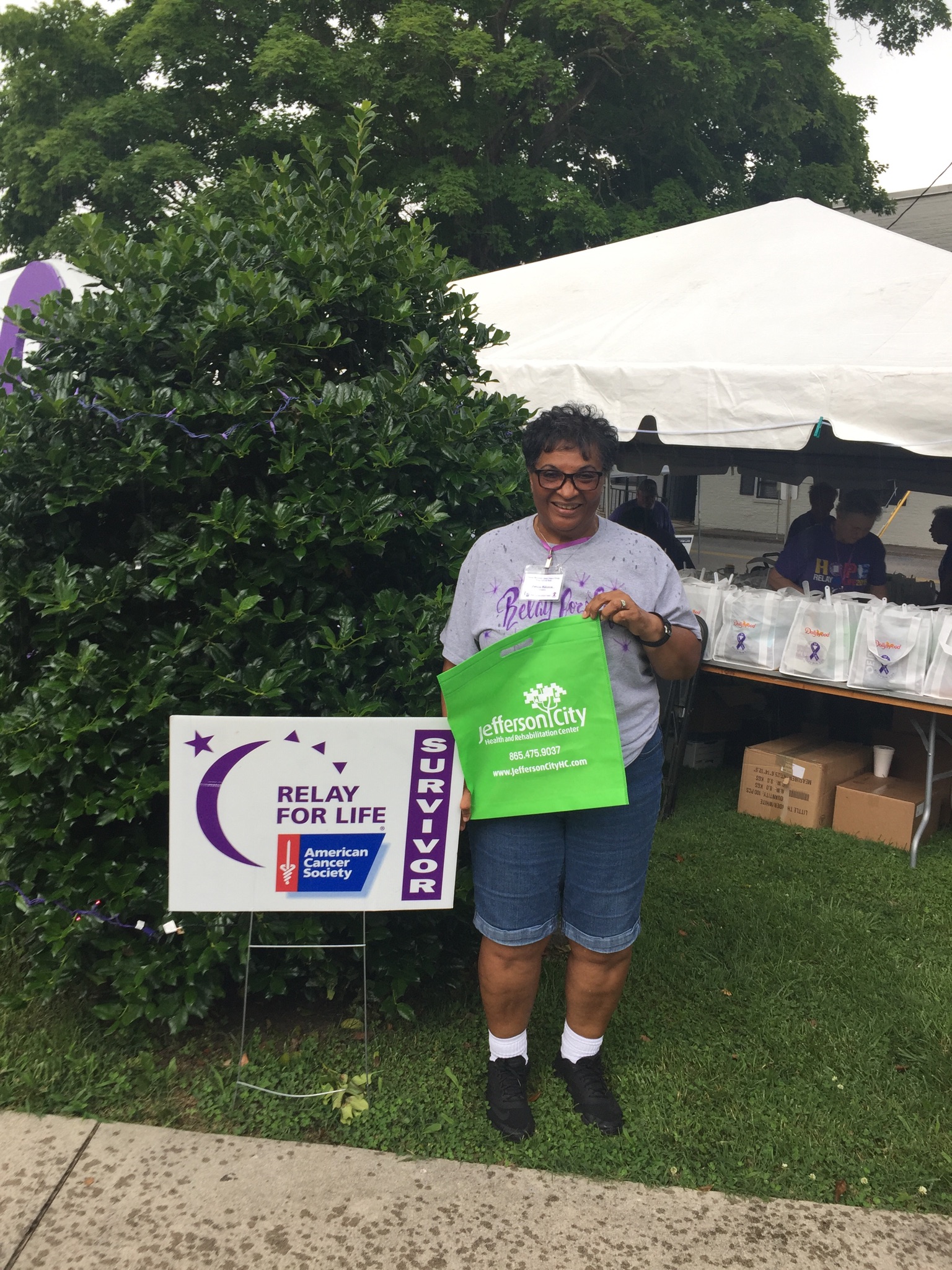 Pat holding up Jefferson City tote bag in front of Relay for Life Sign